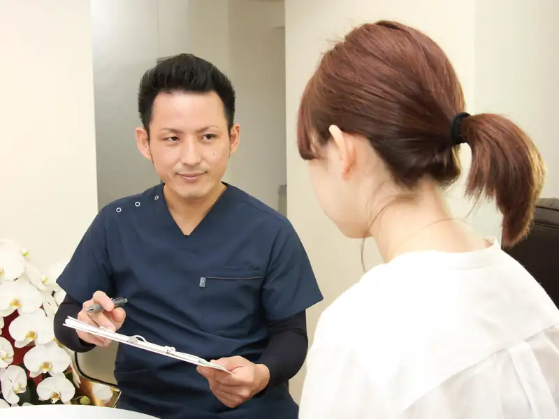 院長の安部が問診票を手に、お話を伺っている様子（院内の相談スペース）