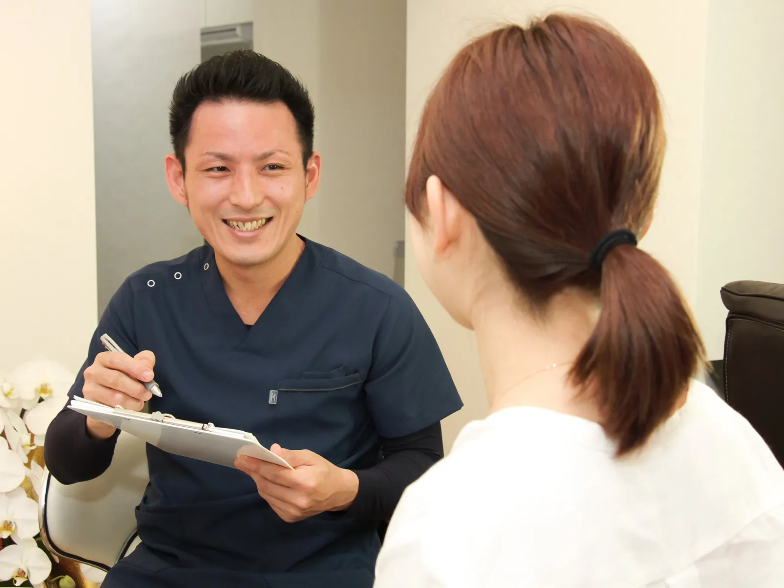 クリップボードを手に、笑顔で話を伺う院長